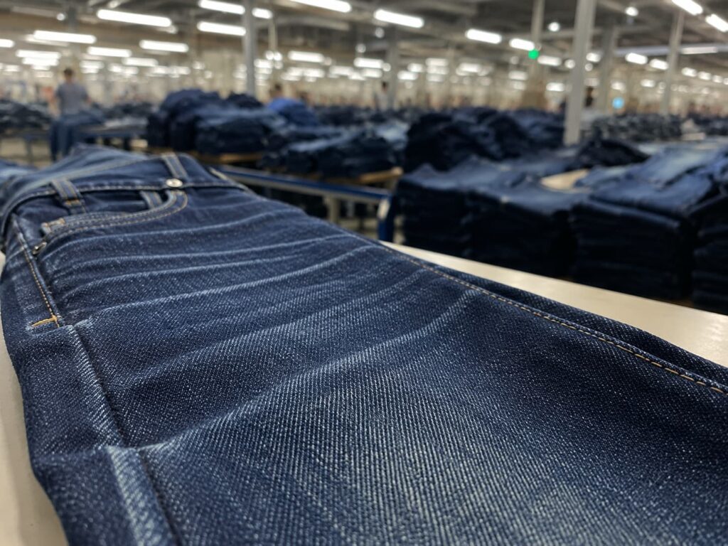 denim sample in sharp focus with bulk production garments blurred behind
